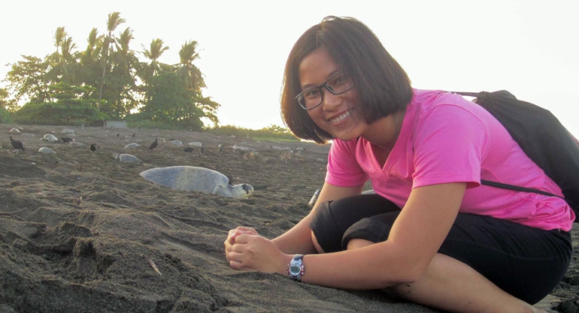 A person leans down to be captured in the frame with a sea turtle behind them. 